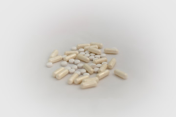 Fototapeta na wymiar Bunch of pills - tablets and capsules - on white background. Selective focus. Light yellow capsules and white tablets are scattered over a white background. Virus cure.