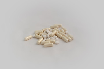 Bunch of pills - tablets and capsules - on white background. Selective focus. Light yellow capsules and white tablets are scattered over a white background. Virus cure.