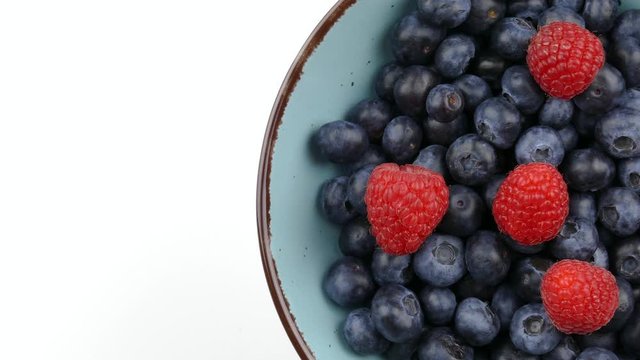fresh blueberry and raspberry fruits in a blue bowl rotating on white copy space top view closeup 4k