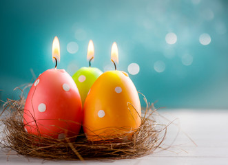 Easter candle eggs in the nest on white table and blurred blue background. Copy space