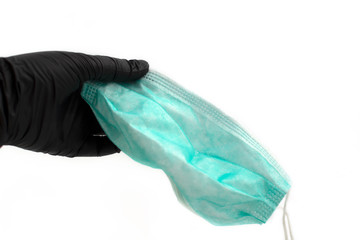 Hand in black latex glove holding green disposable medical face mask. Selective focus. Face protection mask is held by hand in black medical glove at white background. Virus care.