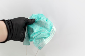Fototapeta premium Hand in black latex glove holding green disposable medical face mask. Selective focus. Face protection mask is held by hand in black medical glove at white background. Virus care.