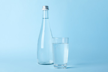 Glass and bottle with water on blue background, space for text