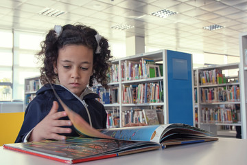Niña leyendo un libro en la mesa de lectura.