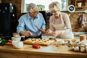 Happy senior couple having fun while preparing bruschetta in the kitchen.