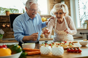 Happy mature husband and wife preparing bruschetta in their kitchen.