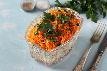 Salad with Korean carrots, ham, eggs, onion and mushrooms in a transparent salad bowl on a light blue background