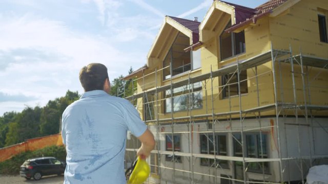 SLOW MOTION, CLOSE UP: Unrecognizable happy architect throws his yellow hard hat in the air after seeing the unfinished house. Young contractor is excited to go on vacation after a long project.