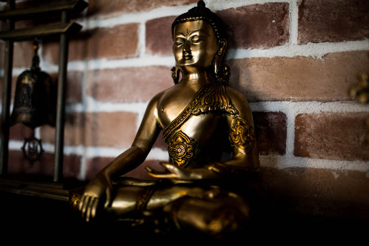 Small Buddha statue in the interior against a brick wall.