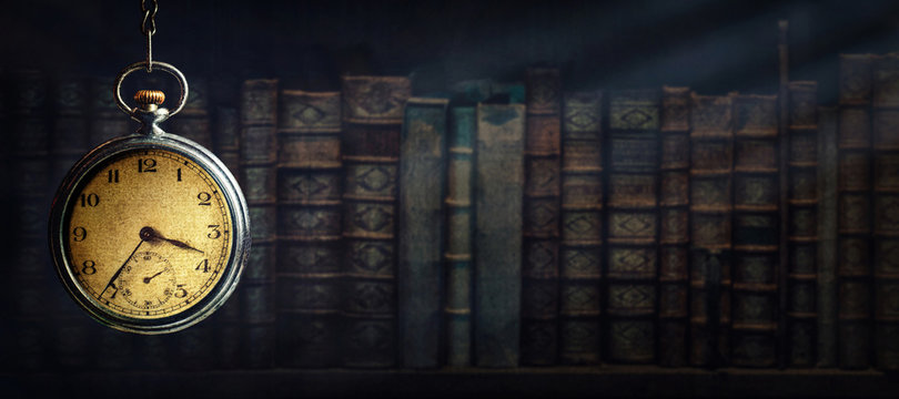 Vintage clock hanging on a chain on the background of old books and sun rays. Old watch as a symbol of passing time. Concept on the theme of history, nostalgia, old age. Retro style.
