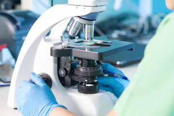 Female professional in uniform, hands in gloves. Work with light or fluorescent microscope in...