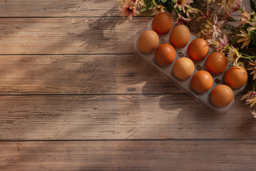 Ten brown eggs and flowers on wooden background. Easter holiday concept. Rustic style. Flat lay, top view, copy space.