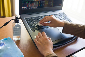 Woman working home office and cleaning her laptop with handkerchief and cologne to protect herself from Corona Virus (COVID-19, COVID19, covid19, covid 19, Coronavirus). Digital nomadism concept.