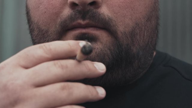 Man smokes real pre-rolled weed joint or medical marijuana or cannabis or hemp, close up