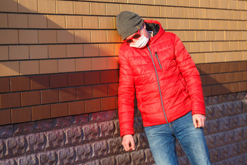 A man in a medical mask leaned against the wall of the house