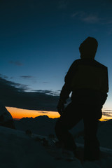 Young men silhouette in winter. A men watch the sunset in the Swiss alps. Orange and blue light on the peaks.