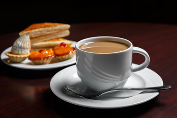 A Cup of coffee on the table against the background of a saucer with cakes