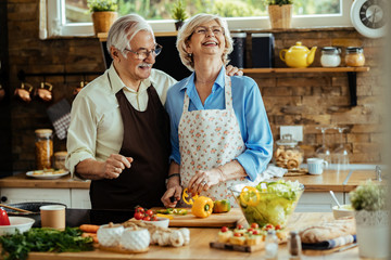 Cheerful senior couple having fun while making healthy meal in the kitchen.