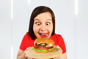 Young fat woman holds hamburger, smiles with opened mouth