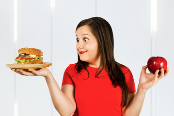 Portrait confused choice think girl holds burger and red apple and surprised