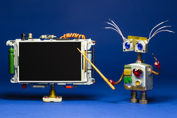 Robot teacher explains theory in the classroom with empty black chalkboard.