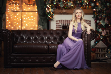 girl in purple evening dress sits on a brown sofa in the New Year's hall