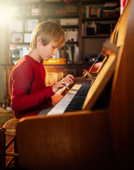 Young boy playing the piano in a sunny living room