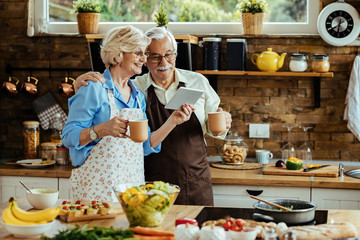 Happy mature couple drinking coffee and using digital tablet in the kitchen.