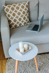 Beautiful stylish interior. The laptop is on the couch, pillow, candles. The cozy corner of the apartment.