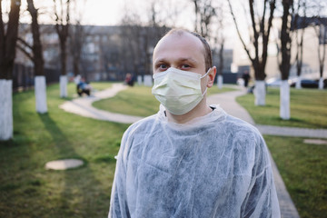 A portrait of young man in yellow protective mask and medical gown on the street. Pandemic...