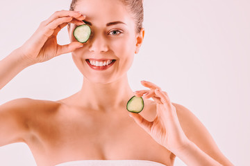 Obraz na płótnie Canvas Beautiful happy girl with perfect smooth face skin posing with cucumber slices isolated on background. Attractive girl beauty model holding cucumbers in hands and smiling. Beauty treatment procedures