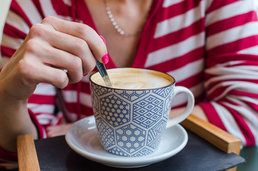 Hand holding spoon mixing a cup of coffee