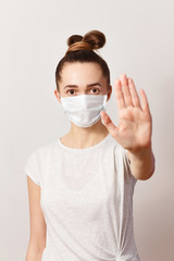 a Caucasian young woman in a medical mask looks at the camera on a white background.. stop the coronavirus