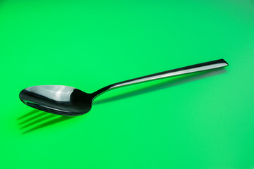 Löffel wirft Schatten einer Gabel auf einen grünfarbenen Hintergrund