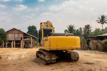 The old yellow backhoe in front of the wooden house in the village. 