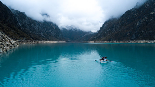 Aerial view on a boat with four tourists floating on turquoise water lake Paron surrounded by mountains in Huaraz, National Park, Peru - highest mountainous range in South America. 