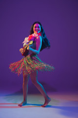 Fabulous Cinco de Mayo female dancer on purple studio background in neon light. Beautiful female model with ukulele, Mexico, Hawaii style. Celebration, holiday, music, beauty and fashion concept.