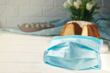 Medical blue protective disposable mask on a background of Easter baking. Protection against viruses. The concept of the celebration of Holy Easter in the context of the coronavirus pandemic.