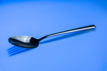 Löffel wirft Schatten einer Gabel auf einen blaufarbenen Hintergrund