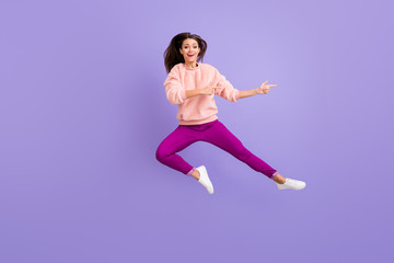 Fototapeta na wymiar Full length photo of cheerful lady jumping high indicating fingers empty space amazing sale wear casual fluffy pullover pants shoes isolated purple color background