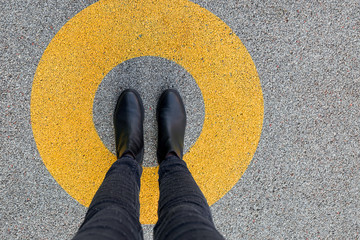 Black shoes standing in yellow circle on the asphalt concrete floor. Comfort zone or frame concept....