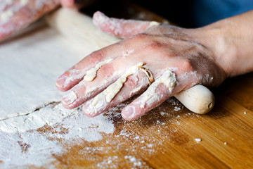 female hands using a rolling pin to pave a dough over a wooden board dirty with flour.