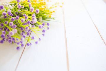 The beautiful plastic spring flowers on white wooden background.