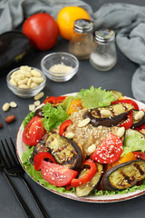 Salad with eggplant, tomato, paprika, lettuce, sesame, peanuts paste dressing on dark background, Vertical orientation