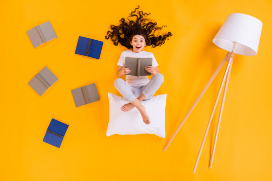 Full length high angle above flat lay view photo of little pupil lady lying floor reading homework book comfy sit on pillow wear pajama pants t-shirt isolated yellow color background