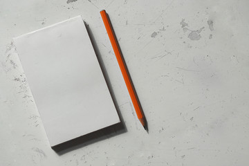white notebook and orange pencil on the table, top view 