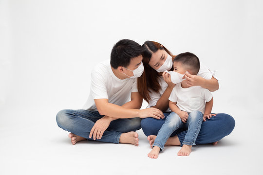 Asian family wearing protective medical mask for prevent virus Wuhan Covid-19 and sitting together on floor isolated white background. Family protection from contaminated air concept