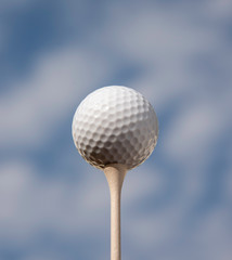 A white golf ball an a tee against a cloudy sky.