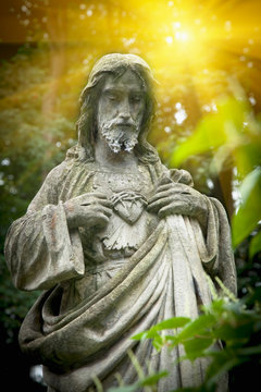 Ancient stone statue of Jesus Christ in the rays of light. Faith, religion, suffering, God concept.