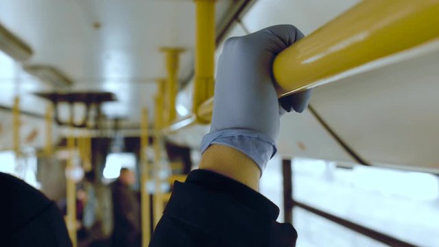 A man rides in a public transport and holds a handrail in his protective medical squirt. Coronavirus infection and epidemic protection concept, pandemic